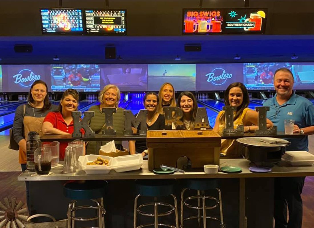 About Our Agency - Kimball Insurance Team Standing Together at a Bowling Alley With Metal Name Plate of Their Agency Name