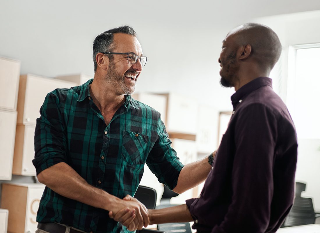 Referrals - Two Friends Shaking Hands While in a Building with Boxes and They are Smiling